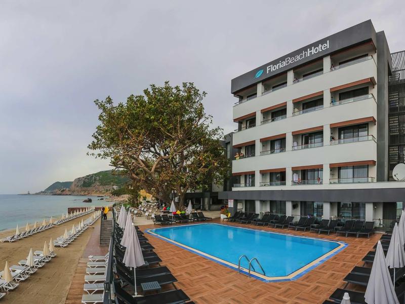 Hotel mit Swimmingpool, Liegestühlen und Meeresblick an einem bewölkten Tag.