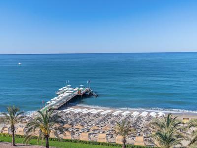 Plage avec transats, palmiers et une longue jetée dans une mer bleue calme sous un ciel clair.