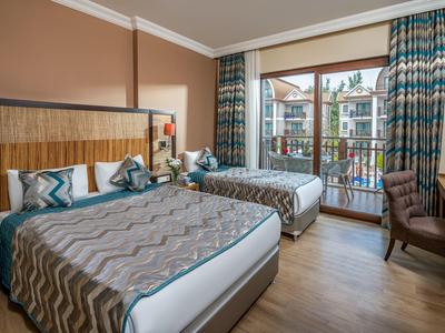 Chambre d'hôtel moderne avec deux lits, balcon et vue sur les bâtiments environnants.