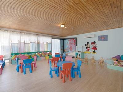 Salle pour enfants avec tables et chaises colorées, tapis de jeu et décorations murales