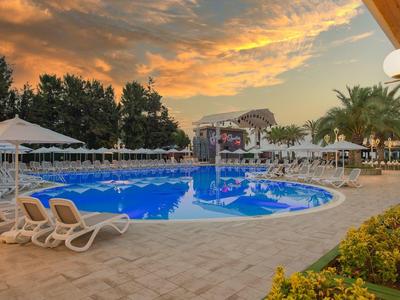 Piscine extérieure avec chaises longues et parasols au coucher du soleil dans un complexe hôtelier.