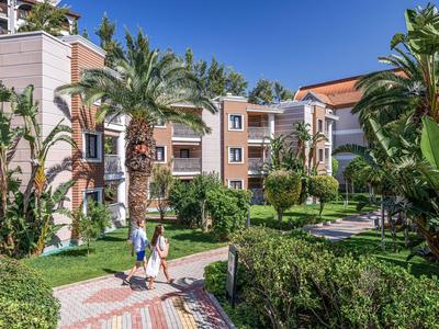 Complejo hotelero con plantas tropicales, palmeras y dos personas caminando por un camino pavimentado.