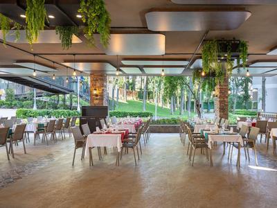 Restaurante moderno y abierto con suelo de madera, mesas blancas, plantas verdes y vista al jardín.
