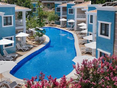 Complejo hotelero moderno con piscina azul, sombrillas blancas y flores coloridas en primer plano.