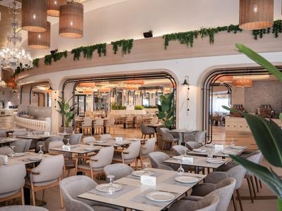 Restaurante de hotel moderno y luminoso con áreas de asientos cómodas y plantas verdes decorativas.