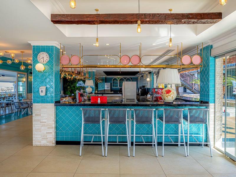 Espace bar d'hôtel moderne avec carrelage turquoise, quatre tabourets de bar et terrasse ouverte