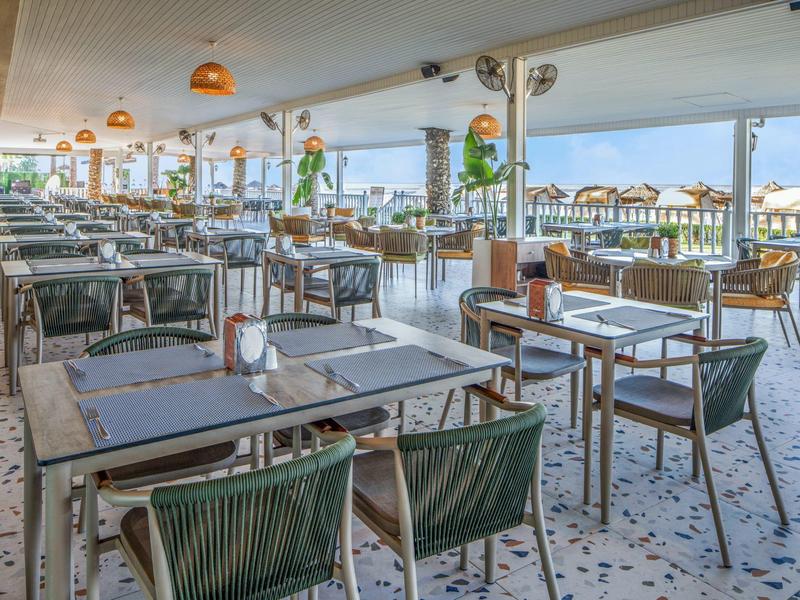 Espace de restauration ouvert avec tables dressées offrant vue sur la plage et la mer.