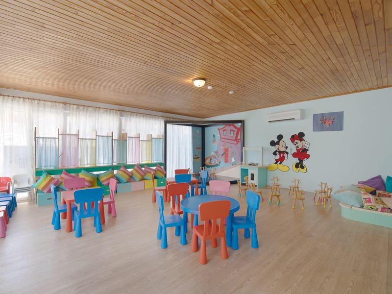 Salle pour enfants avec tables et chaises colorées, tapis de jeu et décorations murales