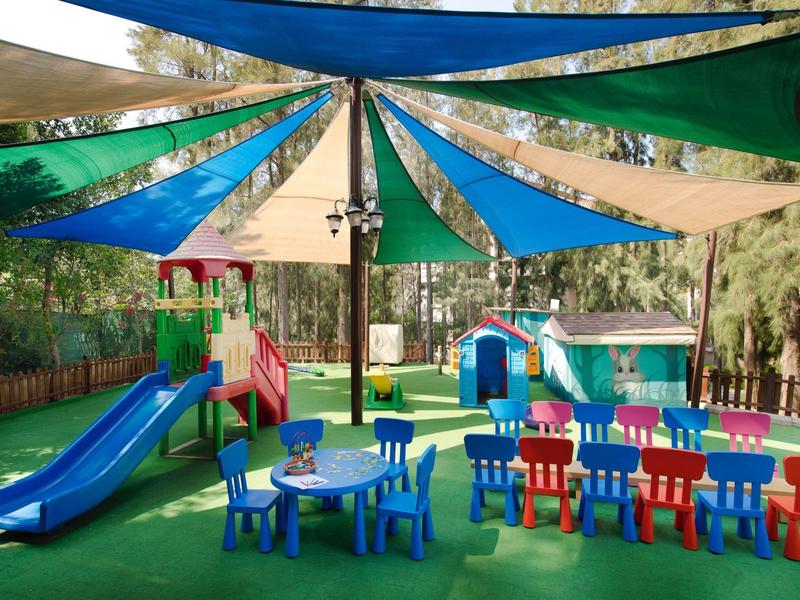 Aire de jeux colorée pour enfants avec toboggans et tables sous un auvent en toile extérieure.