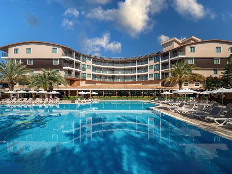 Hôtel avec grande piscine, chaises longues et palmiers sous un ciel bleu.