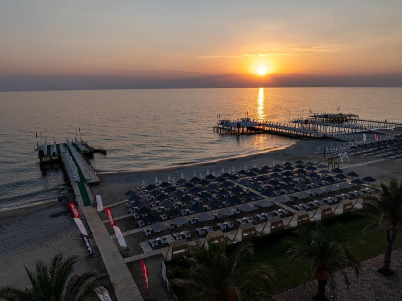 Vue sur une plage avec de nombreuses chaises longues et plusieurs jetées en bois au coucher du soleil.