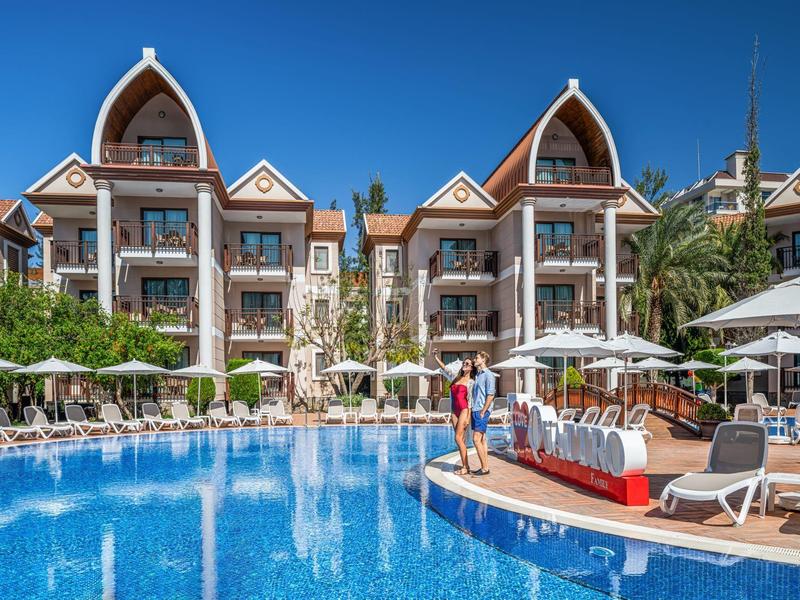 Hôtel avec grande piscine, transats et palmiers sous un ciel dégagé