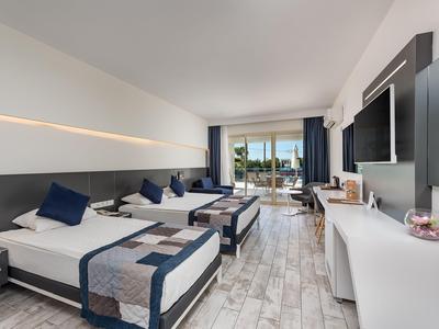 Camera d'hotel moderna con due letti, TV a schermo piatto e balcone con vista mare.