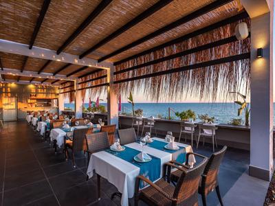 Ristorante all'aperto con tavoli apparecchiati e vista mare al tramonto.