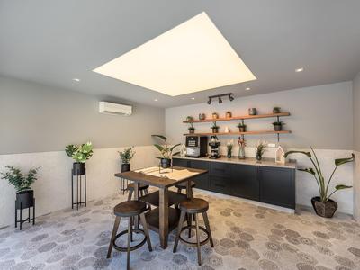 Modern breakfast room with tables, high stools, plants, and coffee machines.