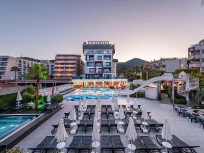 Modern hotel with pool, loungers, and mountains in the background under clear sky.