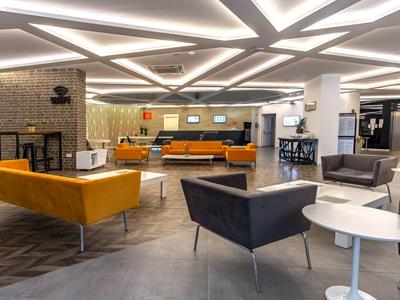Modern hotel lobby with orange sofas, armchairs, and a fireplace in a stylish setting.