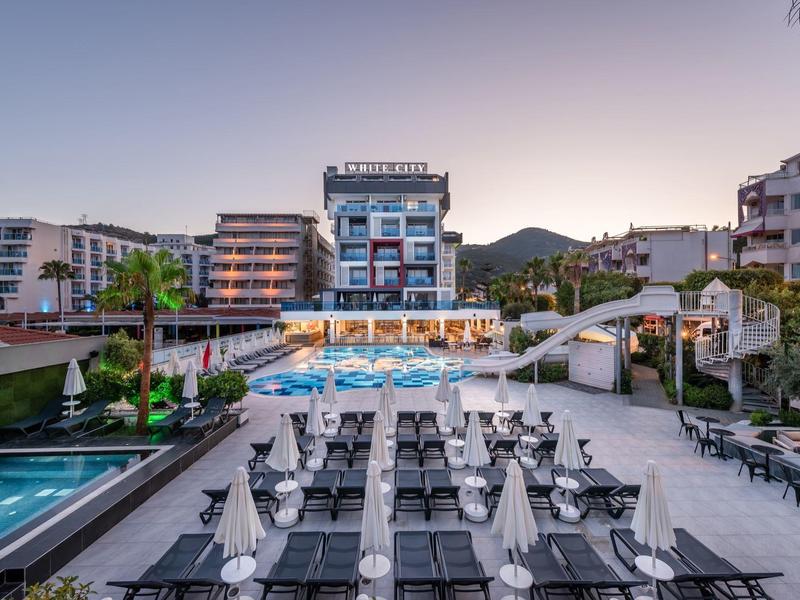 Modern hotel with pool, loungers, and mountains in the background under clear sky.