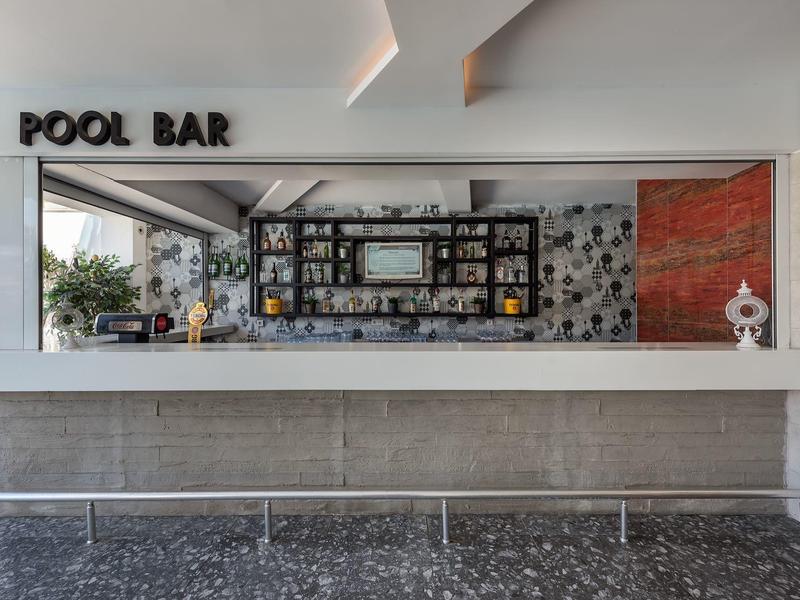 Modern pool bar with mosaic wall and shelves with bottles behind the counter.