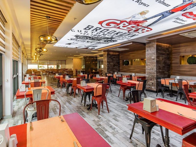 Bright restaurant with red tables, metal chairs, and wooden ceiling with advertisements.