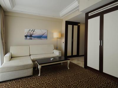 Sala de hotel con sofá blanco, mesa de centro de vidrio y alfombra marrón con patrón elegante.