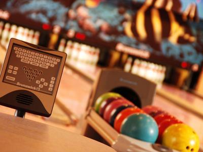 Verschillende kleurrijke bowlingballen liggen op een rek met een scorebord op de voorgrond.