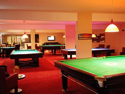 Een gezellige biljartzaal met meerdere tafels en rood tapijt.