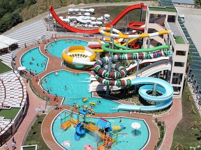 Parque acuático con varias piscinas y toboganes de agua de colores junto a un hotel en un entorno natural.