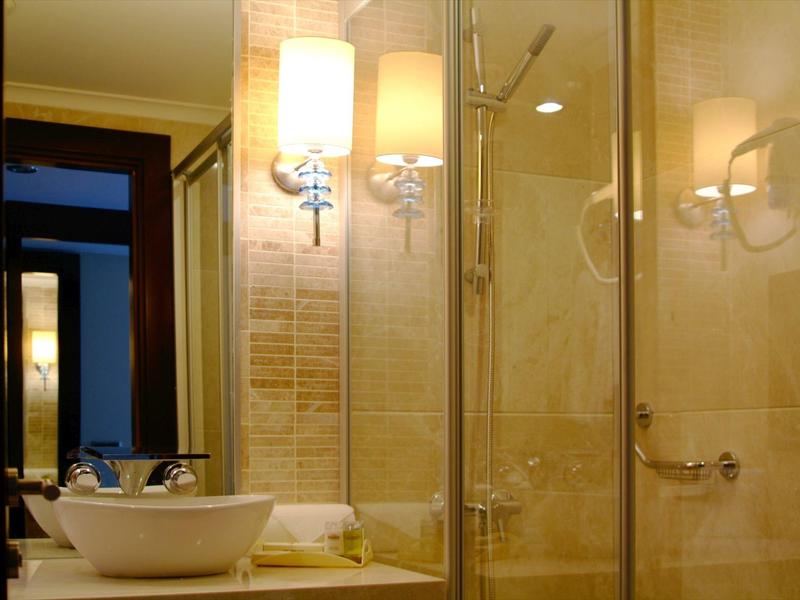 Baño luminoso con lavabo, espejo y lámparas de pared iluminadas junto a la ducha.