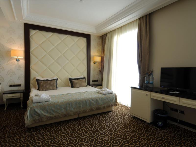 Habitación de hotel moderna con cama grande, televisor de pantalla plana y luz natural por ventanas grandes.