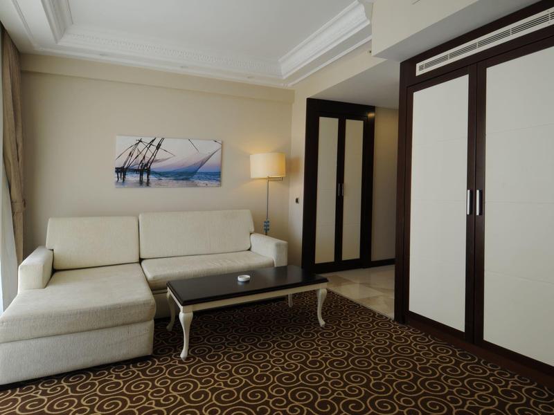 Sala de hotel con sofá blanco, mesa de centro de vidrio y alfombra marrón con patrón elegante.