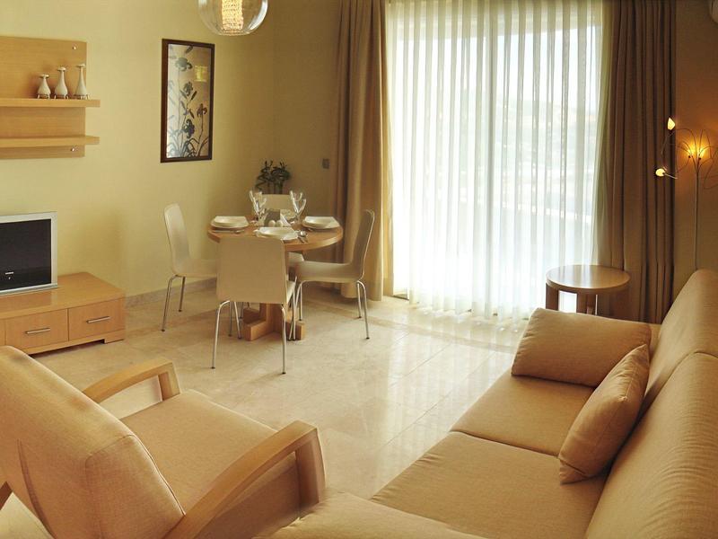 Sala luminosa con sofá, televisor y gran ventana con cortinas para ambiente acogedor.