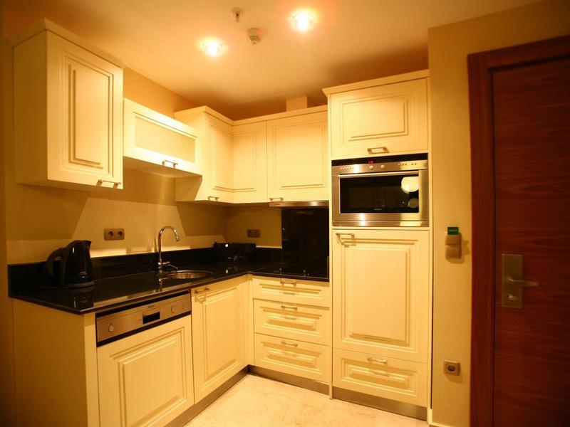 Cocina pequeña de hotel con armarios blancos, encimera negra y electrodomésticos empotrados.