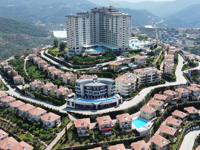 Gran complejo hotelero en una colina con muchas viviendas y vista panorámica de montañas al fondo.