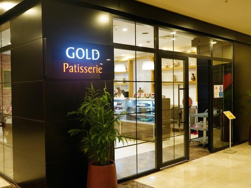 Entrada de una pastelería con paredes de vidrio y plantas en el pasillo del hotel