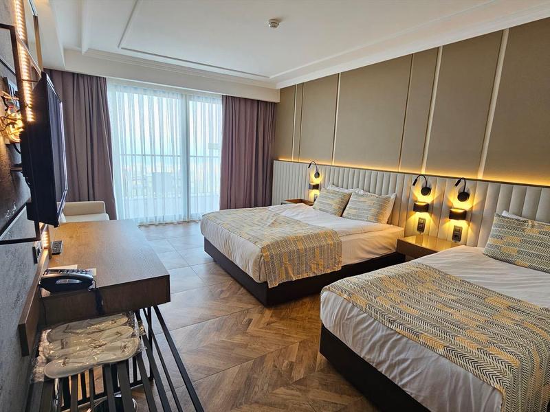 Habitación de hotel moderna con dos camas, suelo de madera y ventana grande con cortinas.