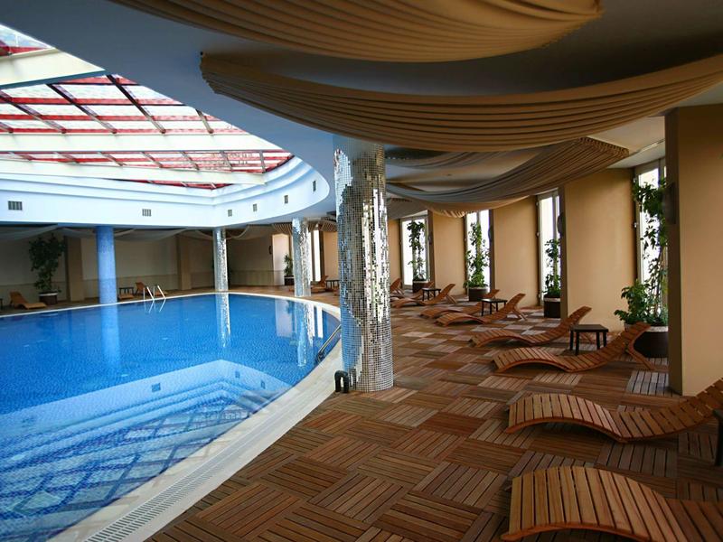 Piscina interior elegante con tumbonas y grandes ventanas que dejan entrar la luz del día.