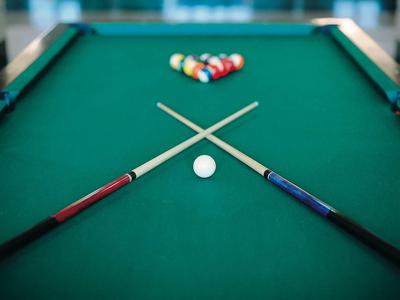 Zielony stół bilardowy z dwoma skrzyżowanymi kijami i bilami w tle.