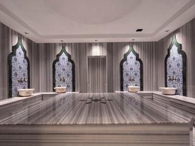 Großer Marmor-Tisch in stilvollem Wellnessraum mit Wänden, Spiegeln und orientalisch geformten Fenstern.