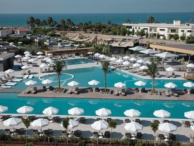 Großer Hotelpool mit vielen weißen Sonnenschirmen, Liegen und Palmen, Blick auf das Meer.