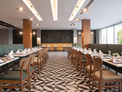 Modernes Restaurant mit geometrischem Bodenmuster, Holztischen und grünen Polstersesseln.