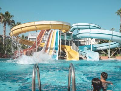 Bunte Wasserrutschen führen in ein blaues Schwimmbecken unter einem klaren Himmel mit Palmen.