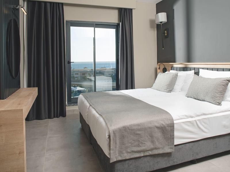 Chambre d'hôtel moderne avec lit double et vue sur la mer depuis la fenêtre.