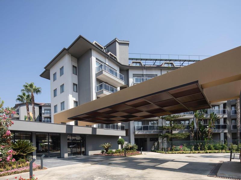 Hôtel moderne avec entrée couverte, plantes et ciel dégagé.
