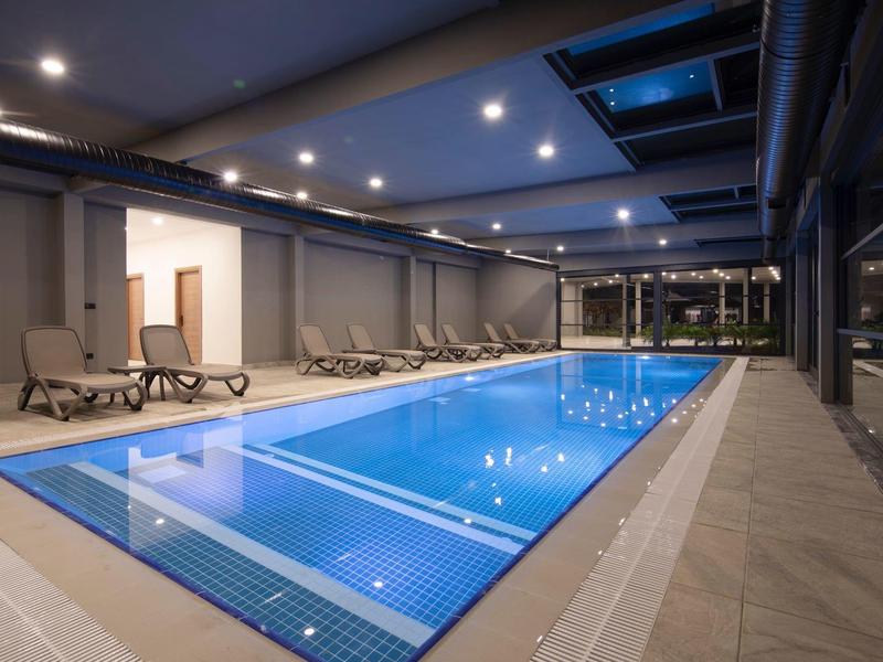 Piscine intérieure moderne avec chaises longues et éclairage LED.