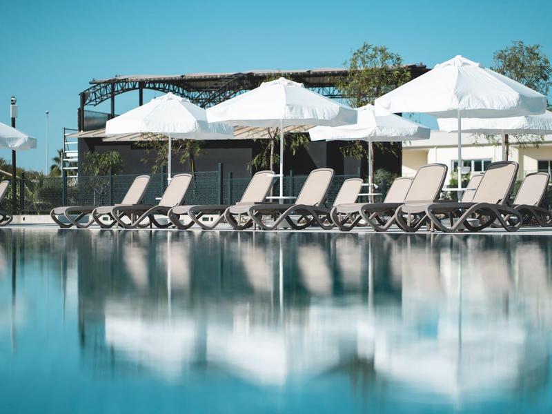 Piscine calme avec chaises longues et parasols blancs sous un ciel bleu clair.