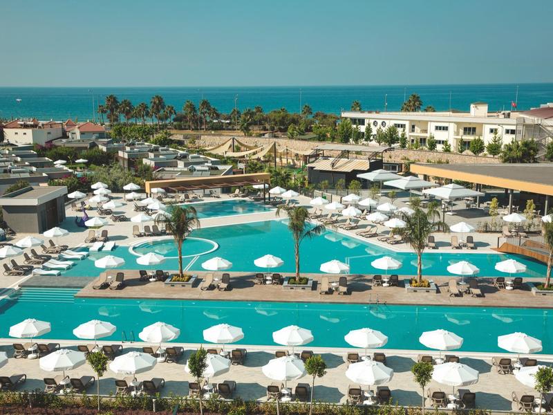 Grand piscine d'hôtel avec de nombreux parasols blancs et palmiers, mer en arrière-plan.