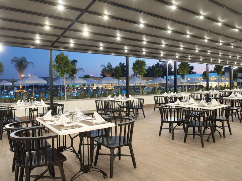 Terrasse de restaurant en plein air avec tables, chaises et vue sur la mer au crépuscule.