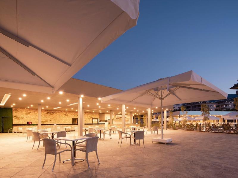 Terrasse d'hôtel éclairée au crépuscule avec parasols blancs et tables vides.