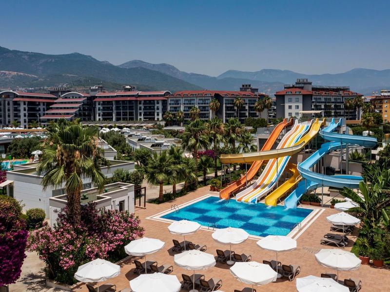 Grand complexe hôtelier avec plusieurs toboggans aquatiques et piscines, entouré de montagnes et de palmiers.